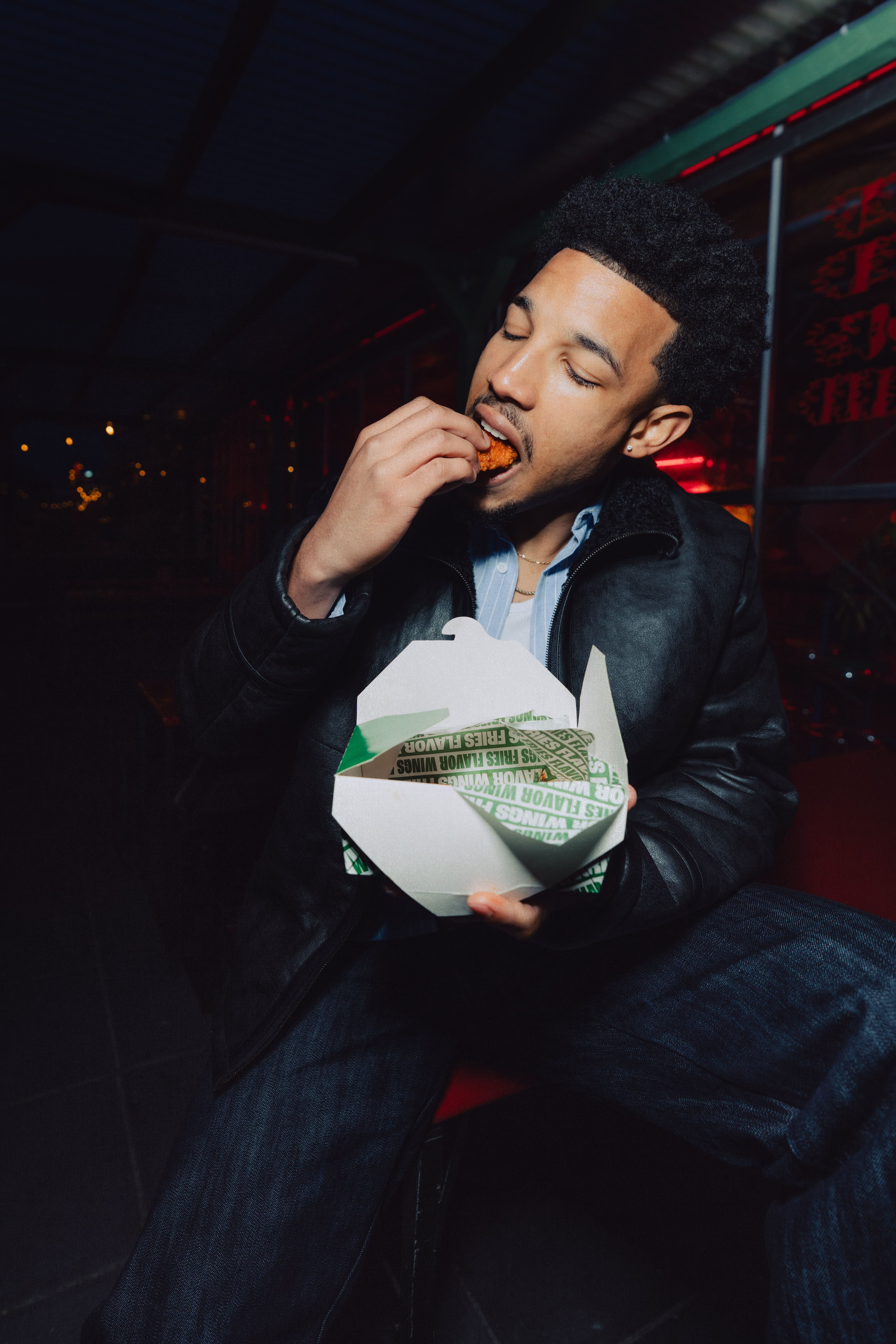 A man eating a chicken wing holding a green basket